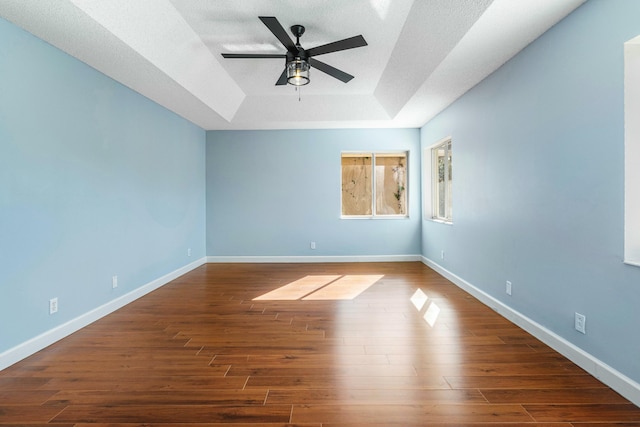 spare room featuring dark wood finished floors, baseboards, a raised ceiling, and ceiling fan