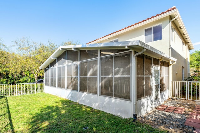 view of home's exterior featuring fence, a tiled roof, stucco siding, a yard, and a sunroom