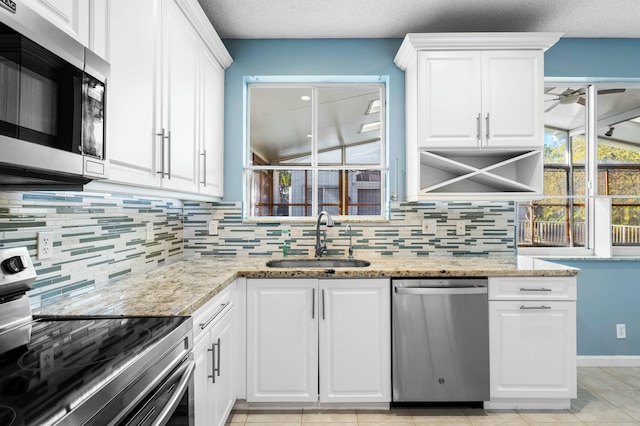 kitchen featuring light stone counters, appliances with stainless steel finishes, white cabinetry, and a sink