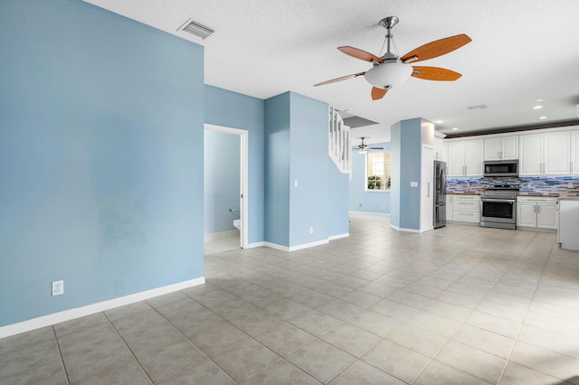 unfurnished living room featuring a textured ceiling, a ceiling fan, visible vents, and baseboards