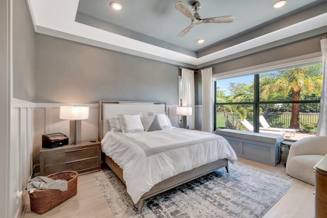 bedroom with a decorative wall, a raised ceiling, ceiling fan, and a wainscoted wall