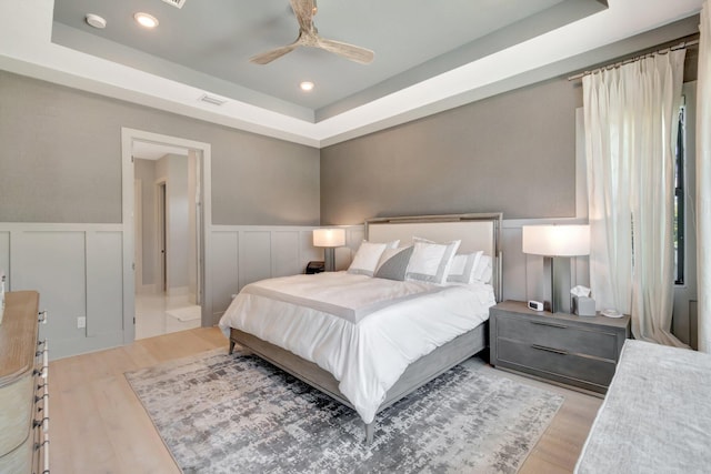 bedroom with a tray ceiling, visible vents, wood finished floors, and wainscoting