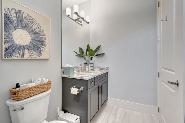 half bath featuring vanity, toilet, and baseboards