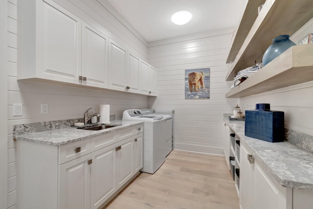 laundry room with light wood-type flooring, washer and clothes dryer, a sink, cabinet space, and wooden walls