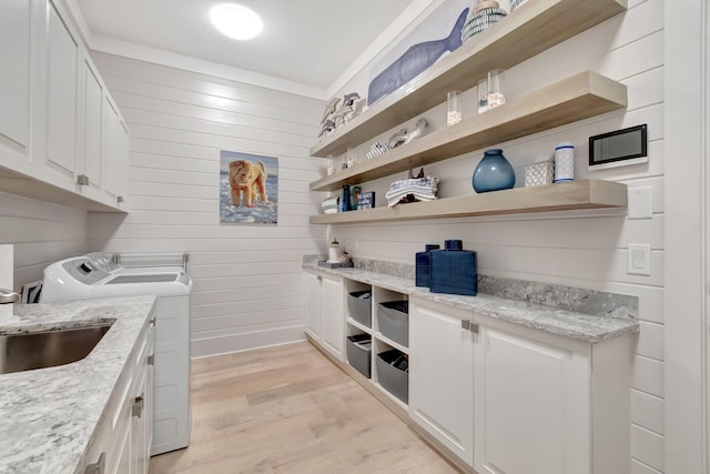 laundry area featuring cabinet space, a sink, light wood-style floors, wood walls, and washer and clothes dryer