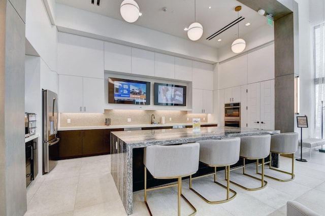 kitchen featuring stainless steel appliances, tasteful backsplash, a breakfast bar area, and a towering ceiling