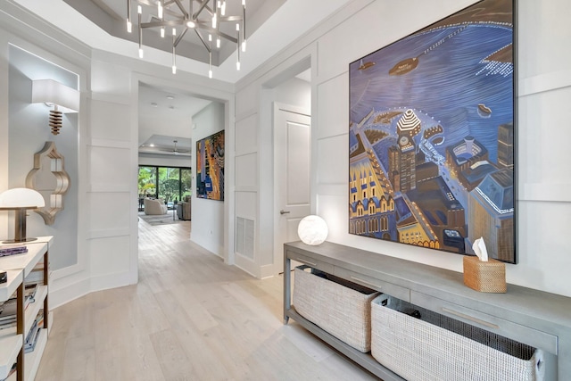 hall with visible vents, light wood-style flooring, a tray ceiling, baseboards, and a chandelier