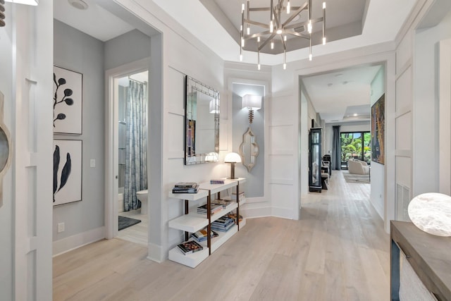 entryway with baseboards, a raised ceiling, light wood-style floors, and a notable chandelier