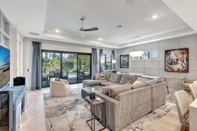 living room featuring a raised ceiling, a decorative wall, visible vents, and light wood-type flooring