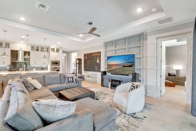 living room with a tray ceiling, a ceiling fan, visible vents, and light wood-type flooring