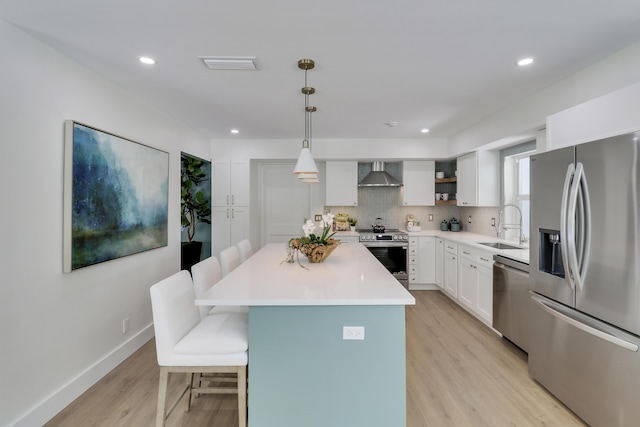 kitchen with a sink, stainless steel appliances, a kitchen bar, wall chimney exhaust hood, and backsplash