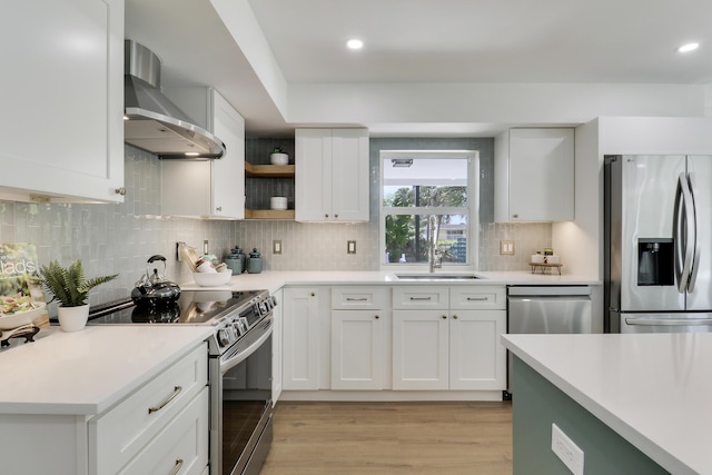 kitchen with a sink, stainless steel appliances, wall chimney exhaust hood, and light countertops