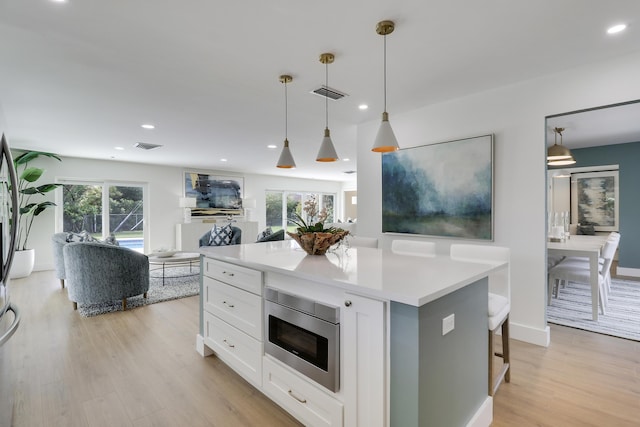 kitchen with visible vents, stainless steel microwave, white cabinetry, light wood finished floors, and light countertops