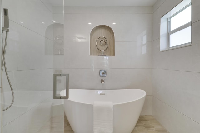 bathroom with a soaking tub and tile walls