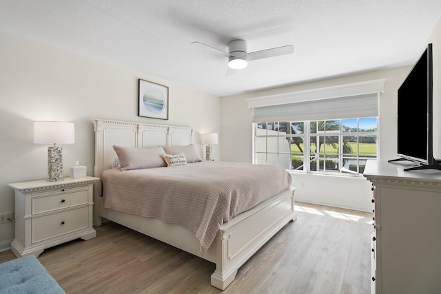 bedroom featuring a textured ceiling, baseboards, light wood-type flooring, and ceiling fan