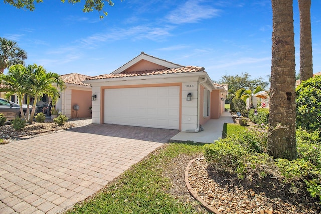 mediterranean / spanish-style home with stucco siding, a tile roof, decorative driveway, and a garage