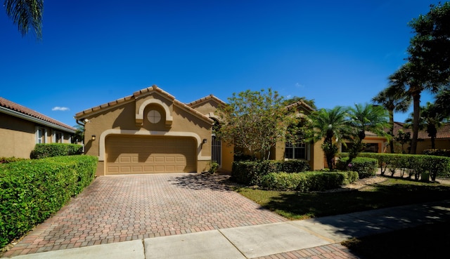 mediterranean / spanish home with stucco siding, a tile roof, decorative driveway, and a garage