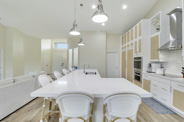 kitchen featuring stainless steel double oven, black electric cooktop, a sink, wall chimney exhaust hood, and tasteful backsplash