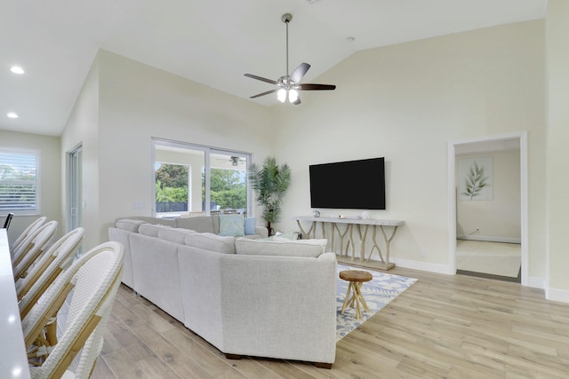 living room with ceiling fan, high vaulted ceiling, light wood-style flooring, and baseboards