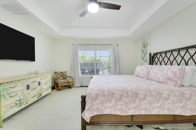 bedroom featuring a ceiling fan, a raised ceiling, visible vents, and light carpet