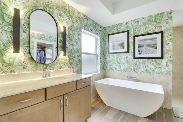 full bathroom with wood finish floors, a wainscoted wall, a freestanding bath, vanity, and wallpapered walls