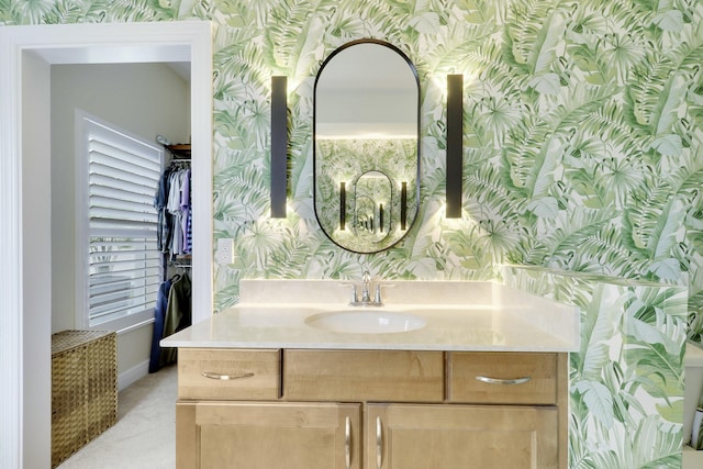 bathroom with wallpapered walls, a spacious closet, baseboards, and vanity