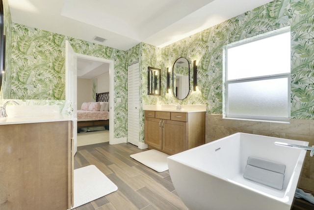 bathroom featuring ensuite bathroom, wood finished floors, vanity, a soaking tub, and wallpapered walls