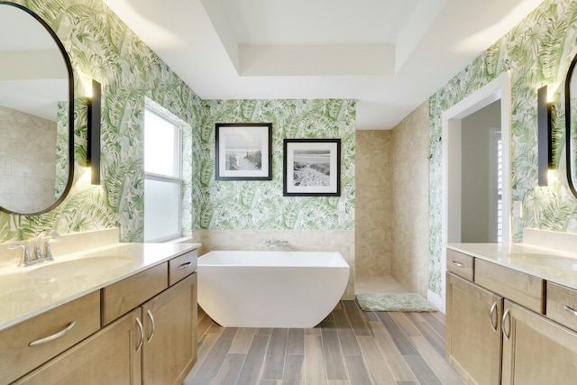 bathroom with wood finish floors, a sink, a freestanding bath, a raised ceiling, and wallpapered walls