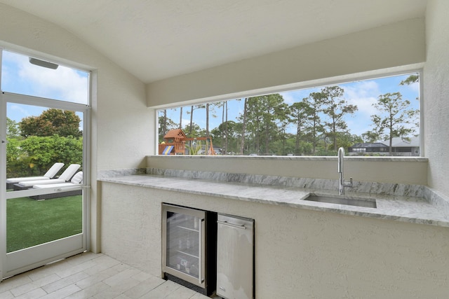 unfurnished sunroom featuring lofted ceiling, wine cooler, wet bar, and a sink