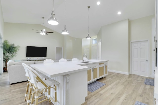 kitchen with light wood finished floors, a kitchen breakfast bar, hanging light fixtures, a large island with sink, and a sink