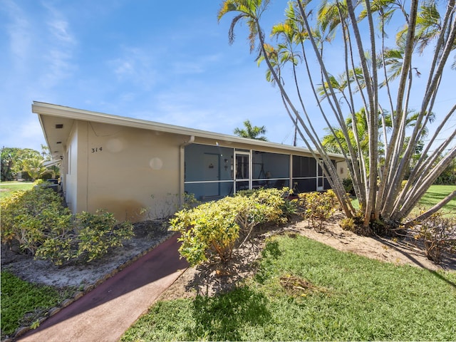 back of property with a lawn, a sunroom, and stucco siding