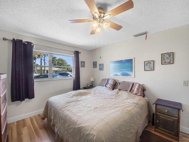 bedroom featuring visible vents, a ceiling fan, a textured ceiling, wood finished floors, and baseboards