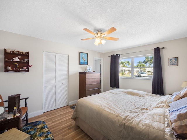 bedroom featuring a textured ceiling, wood finished floors, a ceiling fan, baseboards, and a closet