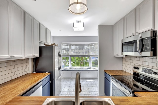 kitchen with a sink, decorative backsplash, appliances with stainless steel finishes, and butcher block counters