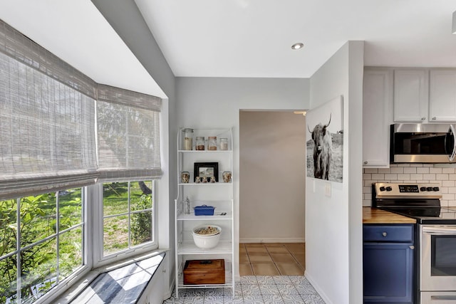 kitchen with light tile patterned floors, appliances with stainless steel finishes, wood counters, blue cabinets, and backsplash