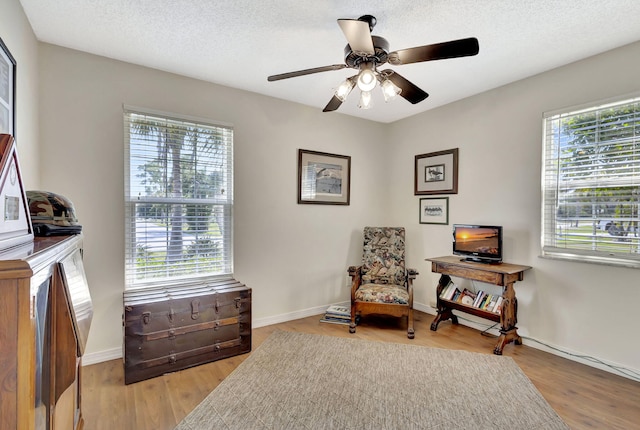 sitting room with light wood-type flooring, baseboards, a textured ceiling, and ceiling fan