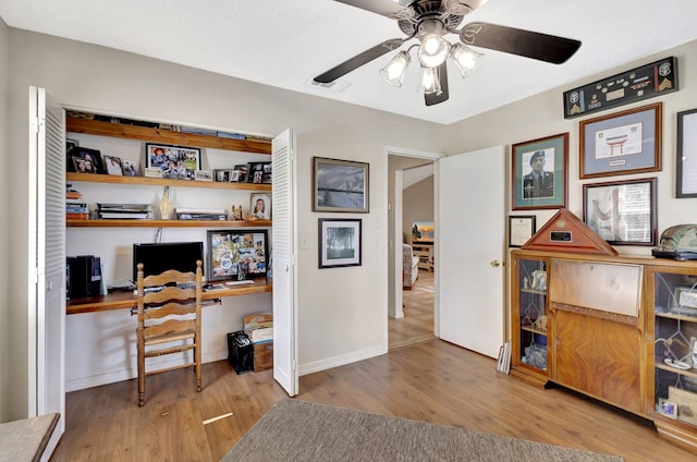 office with a ceiling fan, wood finished floors, baseboards, and built in desk