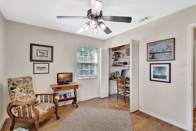 sitting room with light wood-type flooring, visible vents, a textured ceiling, baseboards, and ceiling fan