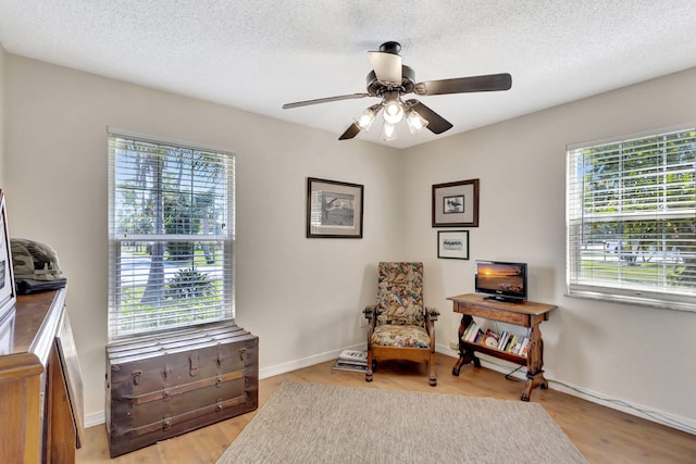 sitting room featuring baseboards, a textured ceiling, light wood-style floors, and a ceiling fan