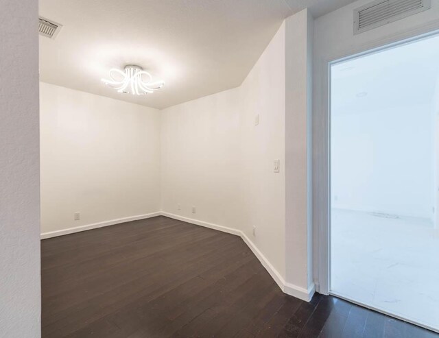 empty room featuring dark wood-style floors, visible vents, and baseboards