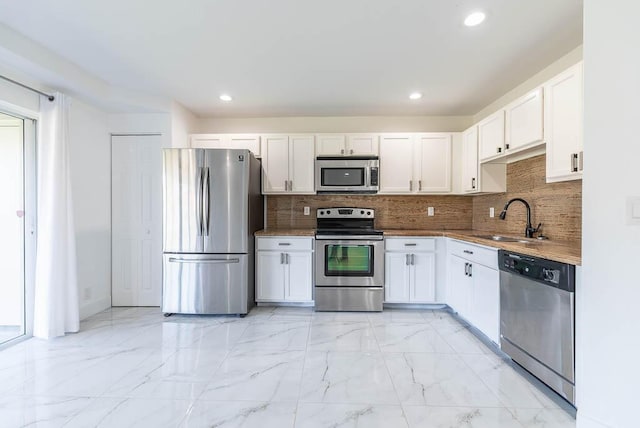 kitchen featuring backsplash, appliances with stainless steel finishes, marble finish floor, white cabinetry, and a sink