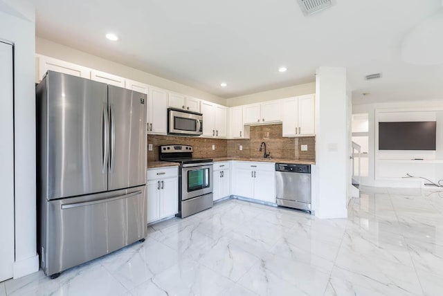 kitchen with a sink, white cabinets, marble finish floor, appliances with stainless steel finishes, and tasteful backsplash