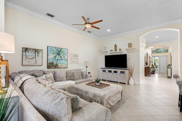 living area featuring arched walkways, light tile patterned floors, visible vents, ornamental molding, and a ceiling fan