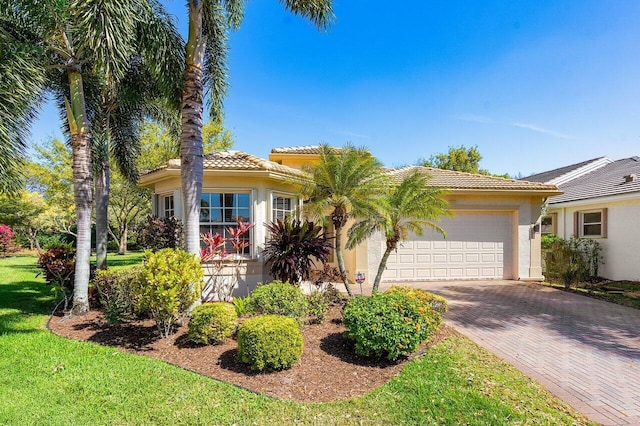 view of front of house with decorative driveway, a tile roof, stucco siding, an attached garage, and a front lawn