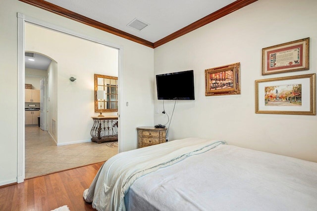 bedroom with baseboards, visible vents, arched walkways, light wood-style flooring, and crown molding