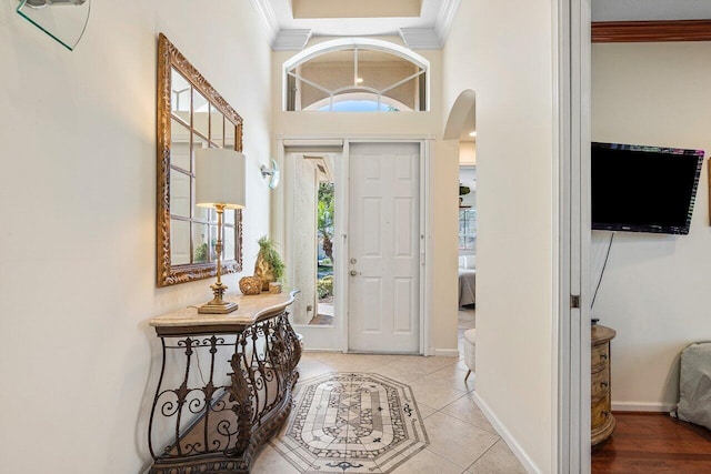 tiled foyer entrance featuring arched walkways, ornamental molding, a towering ceiling, and baseboards