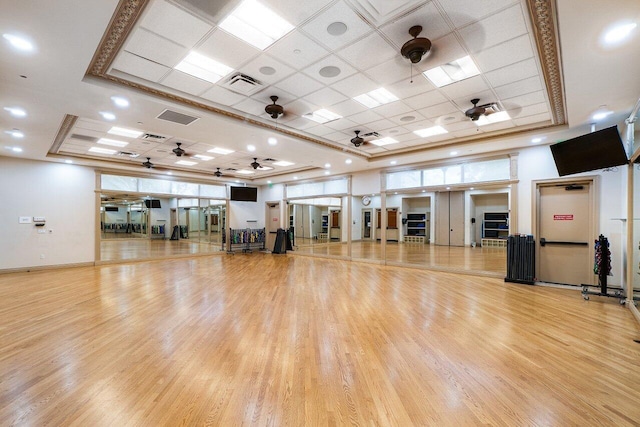 workout room with a ceiling fan, visible vents, a tray ceiling, and wood finished floors