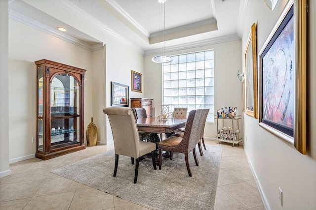 dining area with a raised ceiling, crown molding, baseboards, and light tile patterned floors