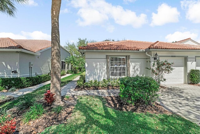 mediterranean / spanish home with a tiled roof, stucco siding, an attached garage, and decorative driveway