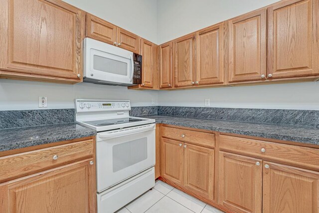 kitchen featuring white appliances, dark countertops, and light tile patterned flooring